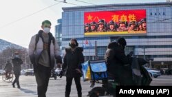 Pejalan kaki melintas di depan layar yang memampang poster Tentara Pembebasan Rakyat China, di Beijing, Senin, 9 Januari 2023. (Foto: Andy Wong/AP Photo)