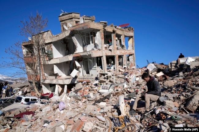 A man sits at his destroyed house in Kahramanmaras, southern Turkey, Wednesday, Feb. 8, 2023. (AP Photo/Hussein Malla)