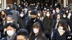 People wear face masks as they leave a train station in Tokyo, Jan. 20, 2023.