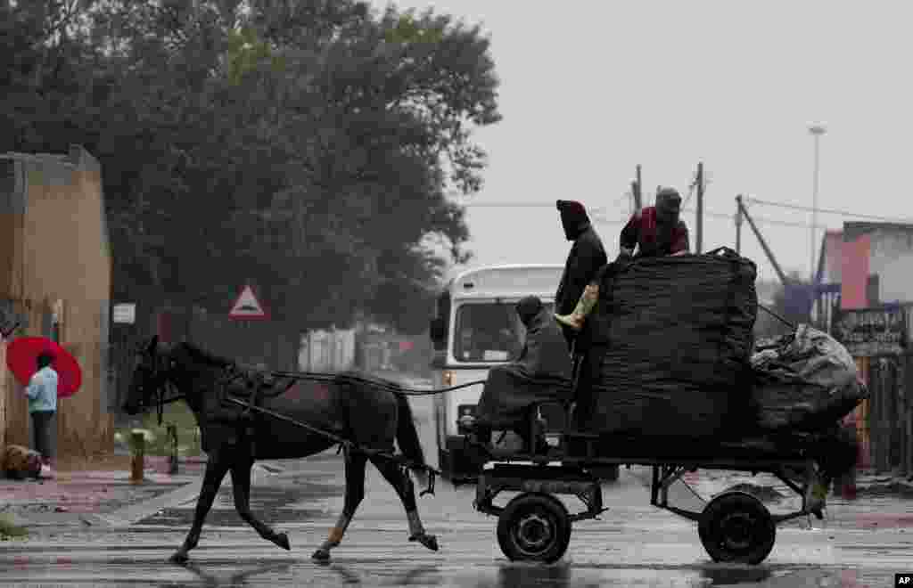 Men ride on a horse-drawn cart carrying sacks filled with recyclable material amid the rain in Katlehong, east of Johannesburg, South Africa.