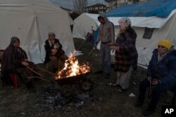 People keep warm next to a fire at a camp for survivors of the earthquake in Gaziantep, Turkey, Friday, Feb. 10, 2023.