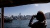 Seorang perempuan mengambil foto dari atas kapal feri di Hong Kong, 2 Februari 2023. Hong Kong menawarkan penerbangan gratis dan voucer untuk merayu wisatawan dalam upaya mengatasi persaingan regional yang sengit. (ISAAC LAWRENCE / AFP)