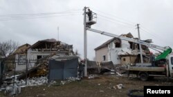 FILE - Employees of a power supplier repair power lines in front of residential buildings damaged by a Russian military strike, in the town of Hlevakha, outside Kyiv, Ukraine, Jan. 26, 2023. 