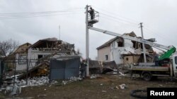 Employees of power supplier repair power lines in front of residential houses damaged by a Russian military strike, in the town of Hlevakha, outside Kyiv, Ukraine, Jan. 26, 2023.