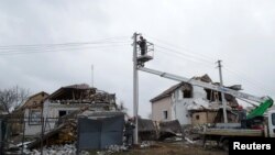 ইউক্রেনের রাজধানী কিয়েভের অদূরে হেলেভাখা শহরে রুশ সামরিক হামলায় ক্ষতিগ্রস্ত আবাসিক ভবনগুলোর সামনে বিদ্যুৎ বিভাগের কর্মীরা বিদ্যুতের লাইন মেরামত করছেন। ২৬ জানুয়ারি ২০২৩। ফাইল ছবি।