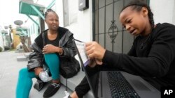 Miesha Clarke sits with her 10-year-old son, Ezekiel West, as he opens his new K12/Stride school loaner laptop computer outside his home in Los Angeles, Jan. 15, 2023.