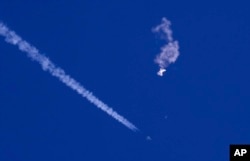 Sisa-sisa balon besar melayang di atas Samudera Atlantik, tak jauh dari pantai Carolina Selatan, sebuah jet tempur dan jejaknya terlihat di bawahnya, 4 Februari 2023. (Foto: via AP)