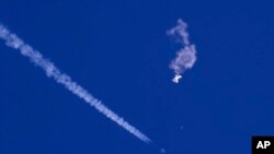 Sisa-sisa balon mata-mata China melayang di atas Samudera Atlantik, tak jauh dari pantai Carolina Selatan, dengan sebuah jet tempur dan jejaknya terlihat di bawahnya, 4 Februari 2023. (Foto: via AP)