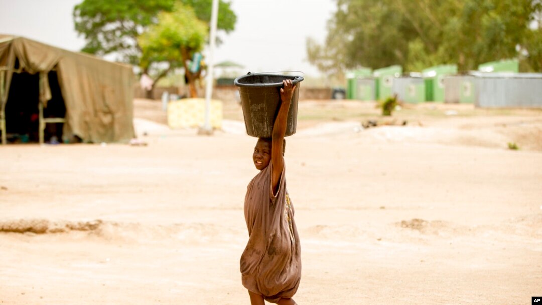 FILE - A child carries a bucket in Yola, Nigeria, April 22, 2016. Droughts, flooding and a shrinking Lake Chad caused in part by climate change is fueling conflict and migration in the region and needs to better addressed, a report said on Jan. 19, 2023.