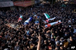 Mourners carry the bodies of eight Palestinians, some draped in the flag of the Islamic Jihad group, during a joint funeral in the West Bank city of Jenin, Jan. 26, 2023.