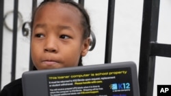 FILE - Ezekiel West, 10, opens up his K12/Stride school loaner laptop computer outside his home in Los Angeles, Jan. 15, 2023.