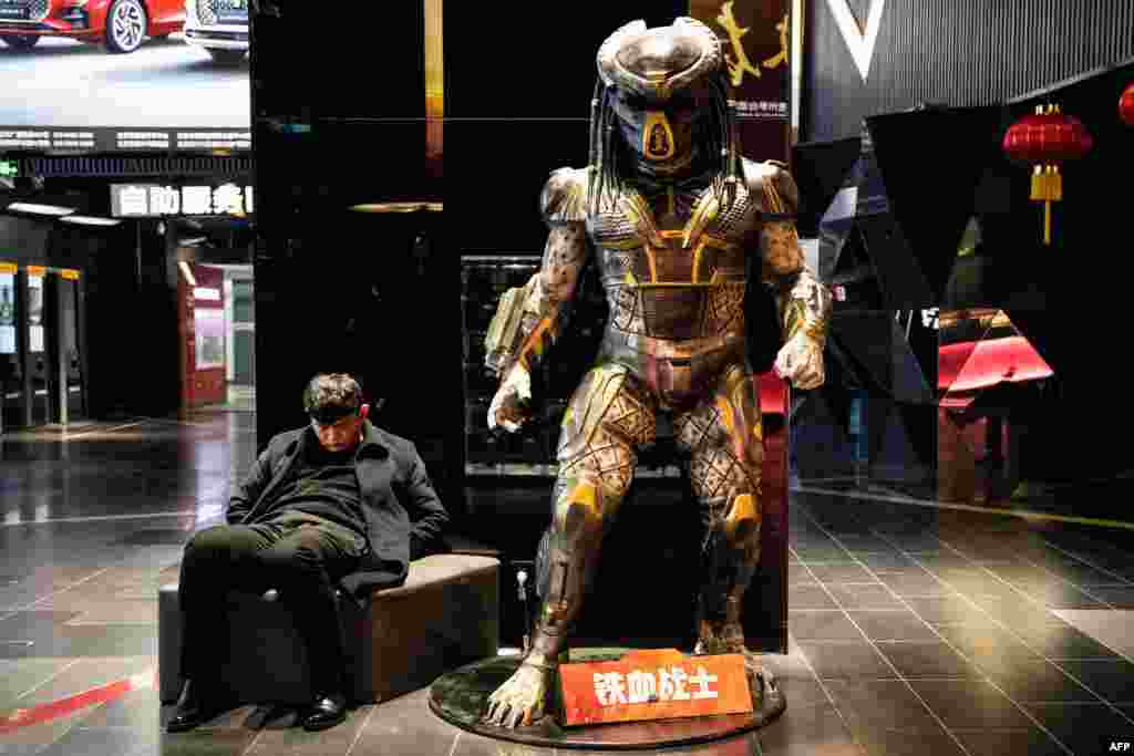 A man naps besides a life-size statue of the Predator film character at a mall in Beijing, China.