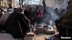 People sit around fire as they are surrounded by debris, following the deadly earthquake in Maras, Turkey, Feb. 11, 2023. In the aftermath of the quake, looters have been stealing from shops and cars.