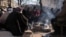 People sit around fire as they are surrounded by debris, following the deadly earthquake in Maras, Turkey, Feb. 11, 2023. In the aftermath of the quake, looters have been stealing from shops and cars.