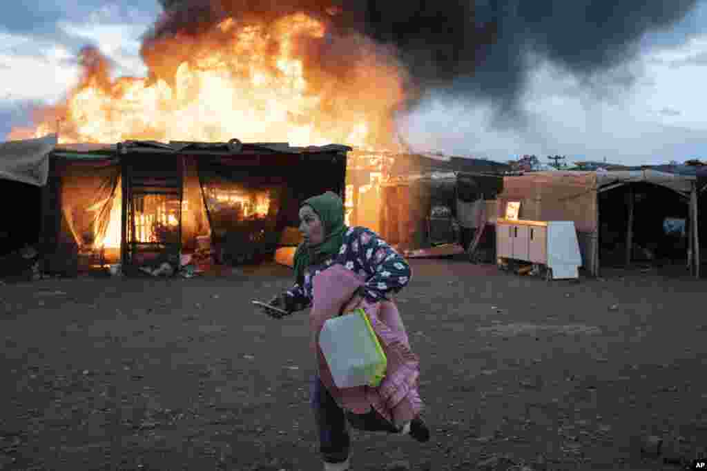 A woman runs past burning shacks during a fire before an eviction by police officers in Almeria, Spain.