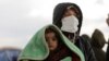 A woman carrying an infant watches as search-and-rescue operations continue days after a deadly earthquake hit Turkey and Syria, in Jindayris, Syria, Feb. 10, 2023.