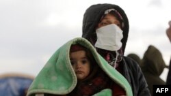 A woman carrying an infant watches as search-and-rescue operations continue days after a deadly earthquake hit Turkey and Syria, in Jindayris, Syria, Feb. 10, 2023.