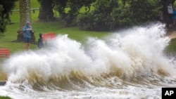 People watch as waves crash against a sea wall at an Auckland beach as a cyclone hits the upper parts of New Zealand, Feb. 12, 2023.