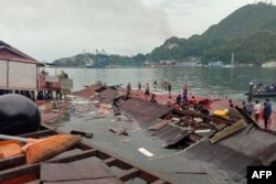 Orang-orang berdiri di atap toko di pelabuhan yang runtuh akibat gempa di Jayapura, Papua, 9 Februari 2023. (FAISAL NARWAWAN / AFP)