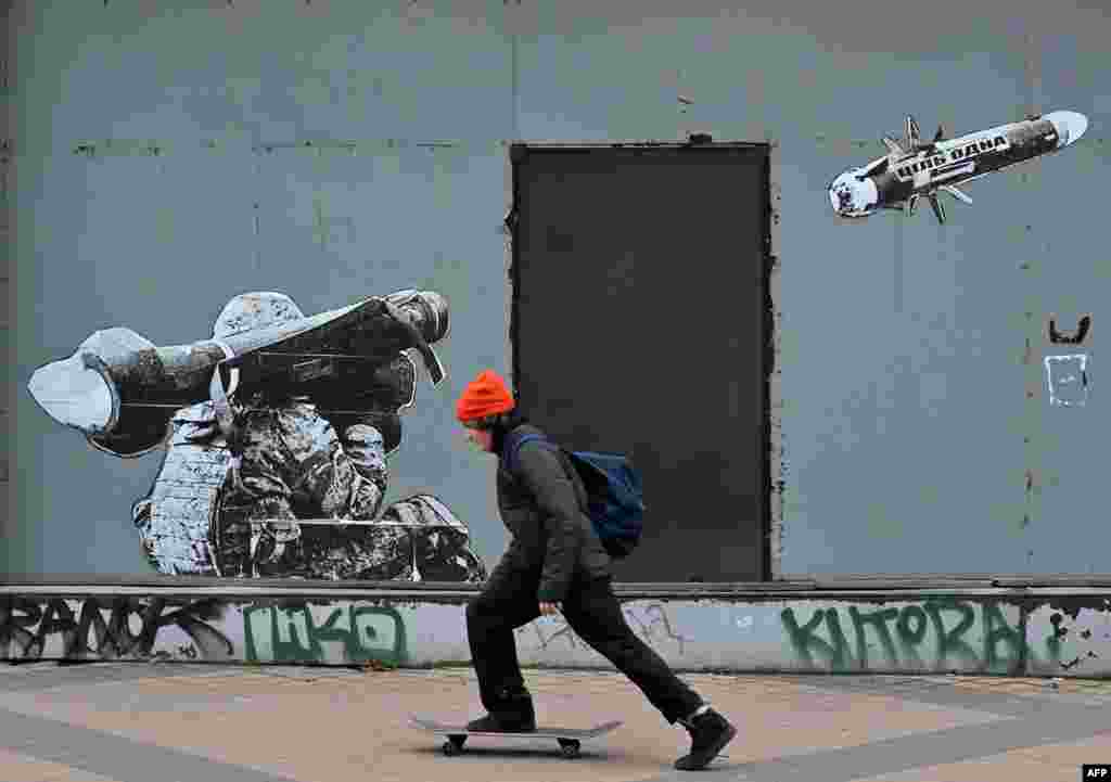 Момче поминува со скејтборд покрај ѕид со графит на кој се гледа како украински војник пука со противтенковски ракетен систем во Киев.
