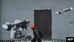 Фото для ілюстрації: хлопець в Києві проїздить повз графіті, де зображено українського військового, який стріляє з "Джавеліна", 25 січня 2023 року (Photo by Sergei SUPINSKY / AFP)