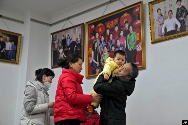 A man carries his grandchild preparing to leave after taking a family photo with his family members at a photo studio in Beijing, Tuesday, Jan. 17, 2023. The world's most populous country has worried for years about an aging population's effect on the economy and society, but the population was not expected to go into decline for almost a decade. (AP Photo/Andy Wong)