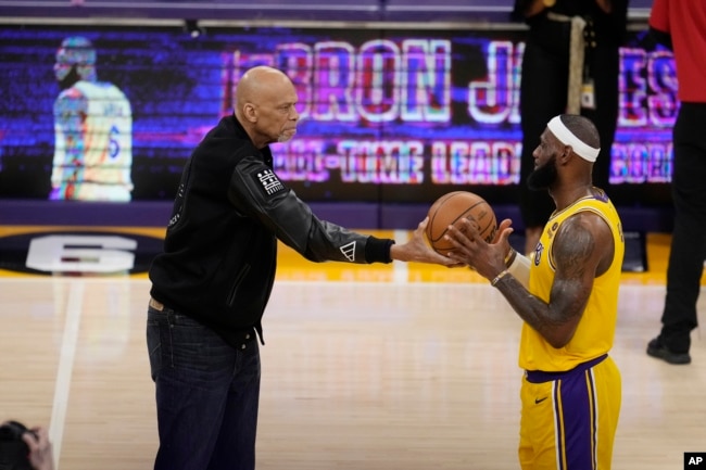 Kareem Abdul-Jabbar, left, hands the ball to Los Angeles Lakers forward LeBron James after passing Abdul-Jabbar to become the NBA's all-time leading scorer. (AP Photo/Marcio Jose Sanchez)