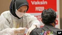 Seorang nakes memberikan suntikan vaksin booster Pfizer COVID-19 kepada seorang pria di pusat vaksinasi di Jakarta, Indonesia, Selasa, 18 Januari 2022. (AP/Dita Alangkara)