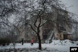 Ljudi noseći torbe prolaze snežnim putem pored uništene zgrade u Bahmutu, u Donjeckoj oblasti, 30. januara 2023.