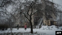 People carrying bags walks along a snowy path past a destroyed building in Bakhmut, in the Donetsk region, on Jan. 30, 2023.