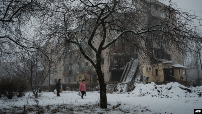 People carrying bags walks along a snowy path past a destroyed building in Bakhmut, in the Donetsk region, on Jan. 30, 2023.