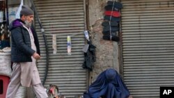 An Afghan refugee cobbler woman, right, repairs a shoe in Peshawar, Pakistan.