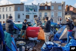 Beberapa pria migran mengatur barang-barang mereka di tenda kemah darurat di luar pusat penerimaan "Petit Chateau" di kota Brussel, Belgia.