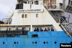 Crew members stand aboard the Akademik Alexander Karpinsky as it arrives in Cape Town harbor, Jan. 28, 2023.