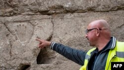 A handout picture provided by the Israel Antiquities Authority on January 25, 2023 shows a Israeli archaeologist pointing at a hand imprint that was discovered carved into a 1,000-year-old dry moat that surrounded Jerusalem's Old City.
