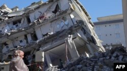 FILE - A woman stand in front of a a collapsed building in Islahiya, in the hard hit region of Gaziantep, Feb. 11, 2023,