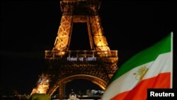 Bendera Iran terlihat berkibar di depan Menara Eiffel di saat menara tersebut menyalakan lampu bertuliskan pesan, "Perempuan, Kehidupan Kebebasan" sebagai bentuk dukungan pada demonstran Iran, di Paris, pada 16 Januari 2023. (Foto: Reuters/Gonzalo Fuentes)