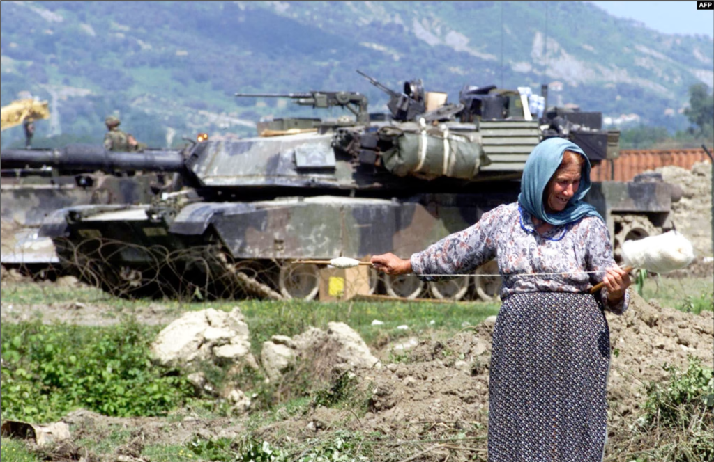 Una mujer albanesa hila lana frente a un tanque M1 Abrams de EEUU, que formó parte de la operación de la OTAN durante el conflicto de Kosovo, en las afueras de la base aérea de Rinas, el 12 de mayo de 1999. Con una tripulación de cuatro (comandante, artillero, cargador y conductor), el Abrams es uno de los tanques más pesados ​​en servicio con casi 62 toneladas métricas.