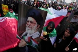 Demonstran membawa bendera besar Iran dan poster Pemimpin Tertinggi Ayatollah Ali Khamenei selama rapat umum tahunan memperingati Revolusi Islam Iran 1979, di Teheran, Iran, 11 Februari 2023. (Foto: AP)