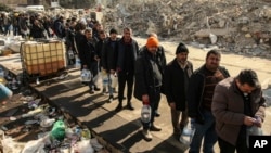People line up for water by collapsed buildings in Kahramanmaras, southern Turkey, Feb. 12, 2023.