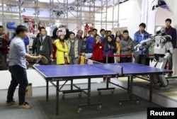 FILE - People look on as a robot (R) plays table tennis with a man during an demonstration at the World Robot Conference in Beijing, China on Nov. 23, 2015.