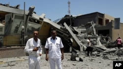 Libyan policemen stand next to a destroyed building that officials said was struck by a NATO airstrike in Tripoli, June 16, 2011