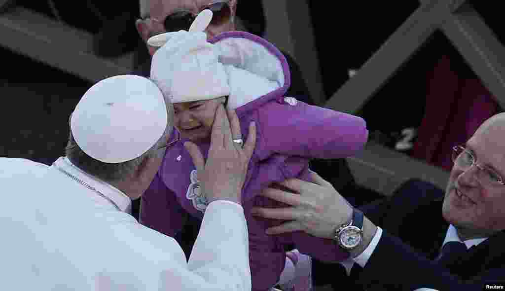 El papa Francisco besa a un niño desde su papamóvil.