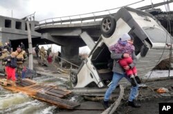 Orang-orang melintasi jalan setapak di bawah jembatan yang hancur saat melarikan diri dari Kota Irpin dekat Kyiv, Ukraina, Senin, 7 Maret 2022. (Foto: AP)