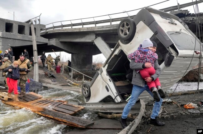 Orang-orang melintasi jalan setapak di bawah jembatan yang hancur saat melarikan diri dari Kota Irpin dekat Kyiv, Ukraina, Senin, 7 Maret 2022. (Foto: AP)