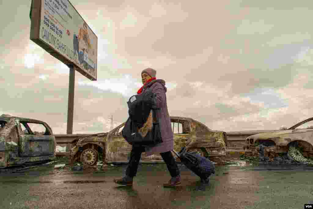 A woman passes by cars that were destroyed by shelling on a bridge that used to link Kyiv to Irpin, in Ukraine, March 8, 2022. (Yan Boechat/VOA) 