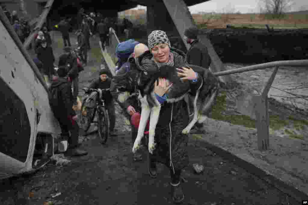 Una mujer sostiene a un perro mientras cruza el río Irpin por un camino improvisado debajo de un puente que fue destruido por un ataque aéreo ruso, mientras ayuda a las personas que huyen de la ciudad de Irpin, Ucrania.