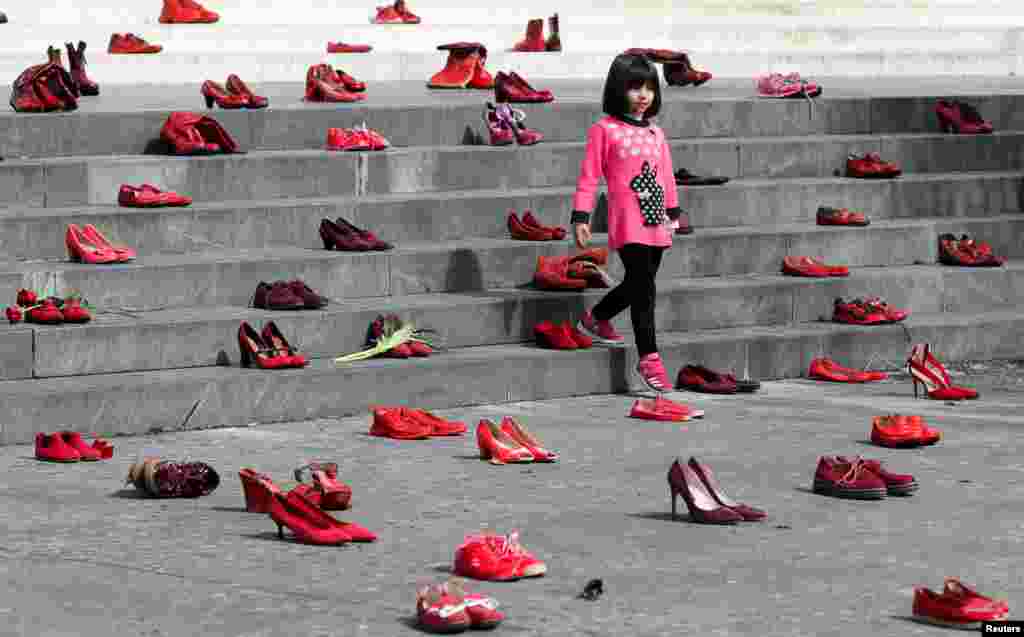 A young girl looks on near artwork of women&#39;s red shoes placed on a staircase, as a way to denounce violence against women, in Tirana, Albania, March 8, 2022.
