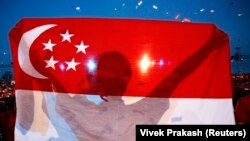 Seorang pria membawa bendera Singapura. (Foto: REUTERS/Vivek Prakash)