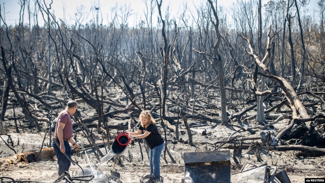 Hector Rivera and Wandi Blanco put water on hotspots on a neighbor's shed next to their home on Whitehead Boulevard after the Adkins Fire tore through the area in Panama City, Florida, U.S. March 5, 2022. 